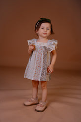Young girl in a patterned dress standing against a brown background
